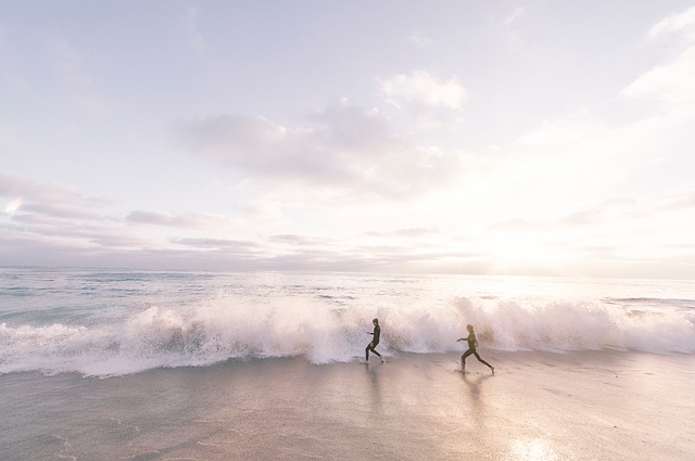 Dvaja ľudia sa naháňajú na pláži pri vlnách.jpg